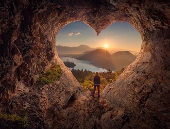 Young woman in heart shape cave towards the idyllic unrise Lone woman enjoying in beautiful mountain nature, celebrating freedom and standing on edge of the cliff against the rising sun. Valentines day concept.